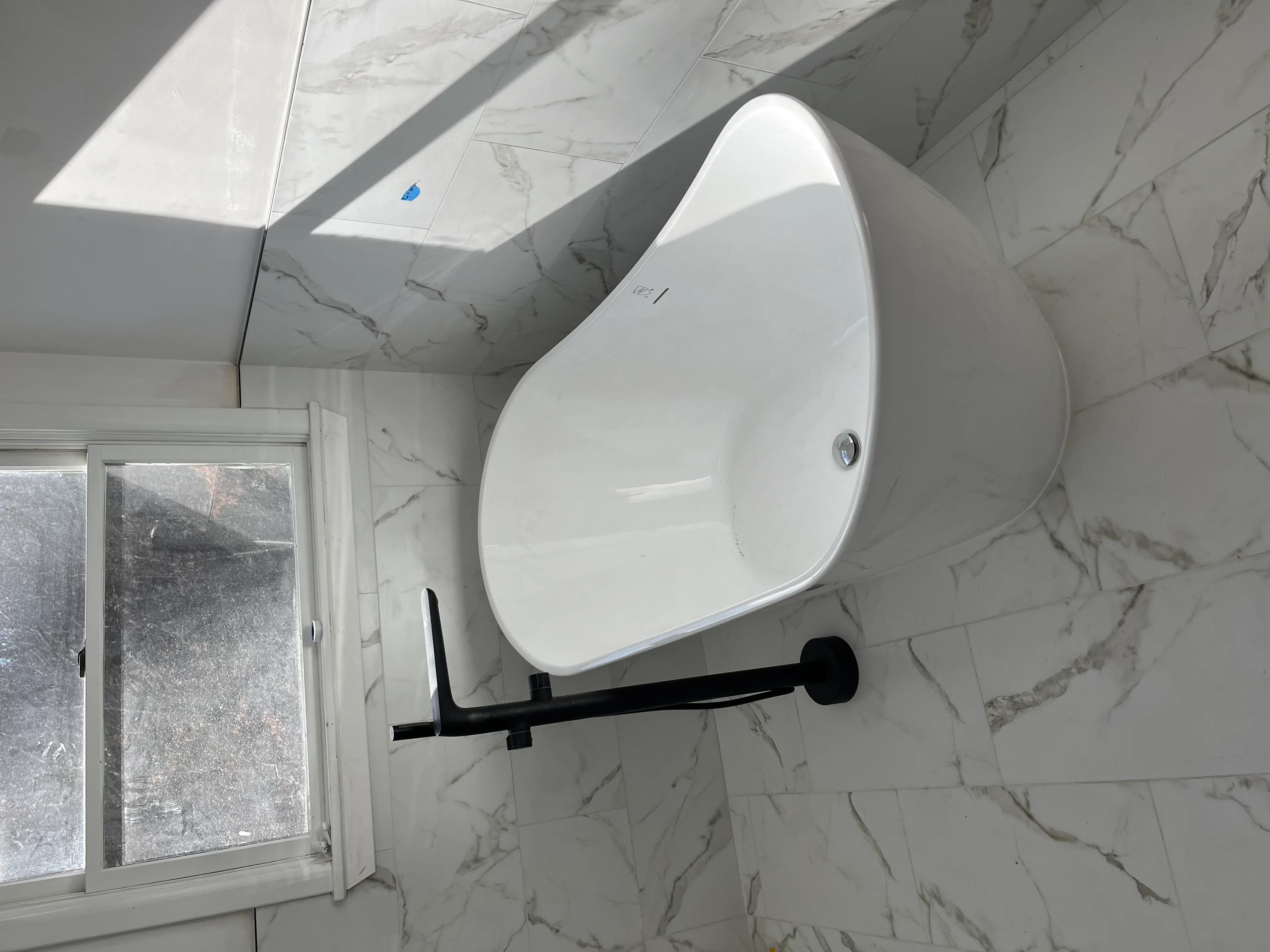 White freestanding soaking tub with black support frame in marble-tiled bathroom with skylights