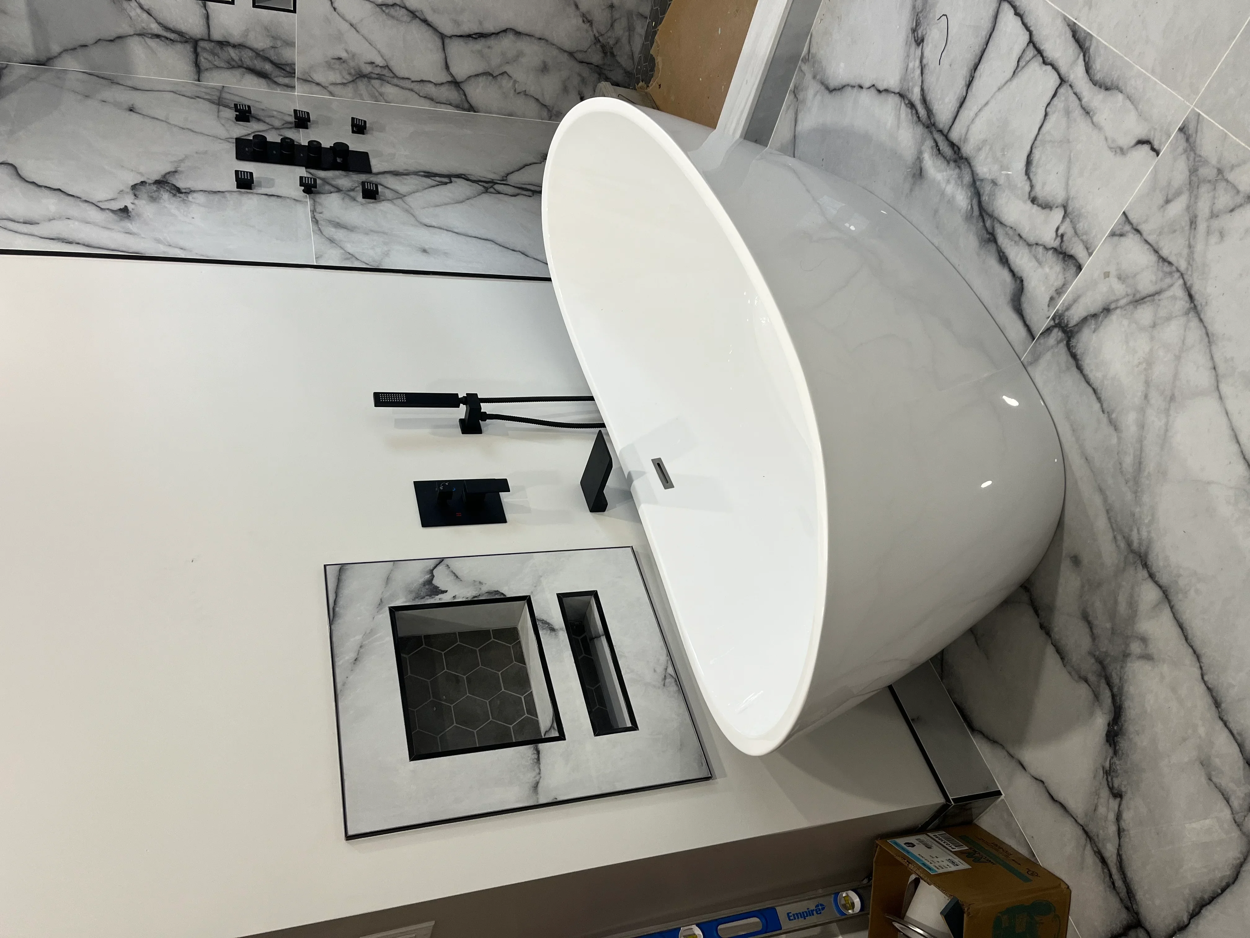 White freestanding tub with black plumbing fixtures and marble tile bathroom installation